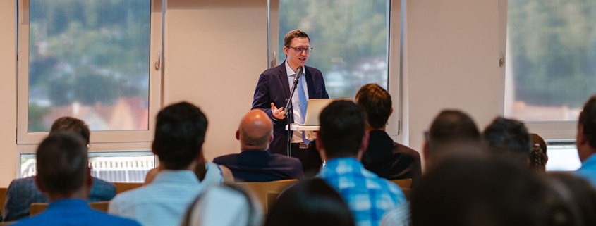 Prof. Dr. Eduard Ferderer hält seine Antrittsvorlesung in Bad Liebenzell. Im Vordergrund sind unscharf die Hinterköpfe der Zuschauerinnen und Zuschauer zu sehen.