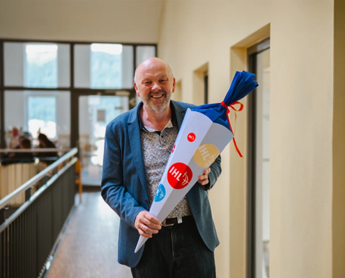 Rektor Volker Gäckle steht lächelnd mit einer Schultüte im Hochschulgebäude