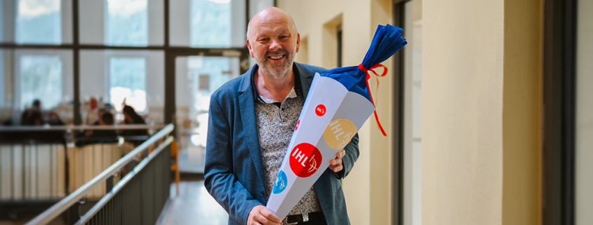 Rektor Volker Gäckle steht lächelnd mit einer Schultüte im Hochschulgebäude