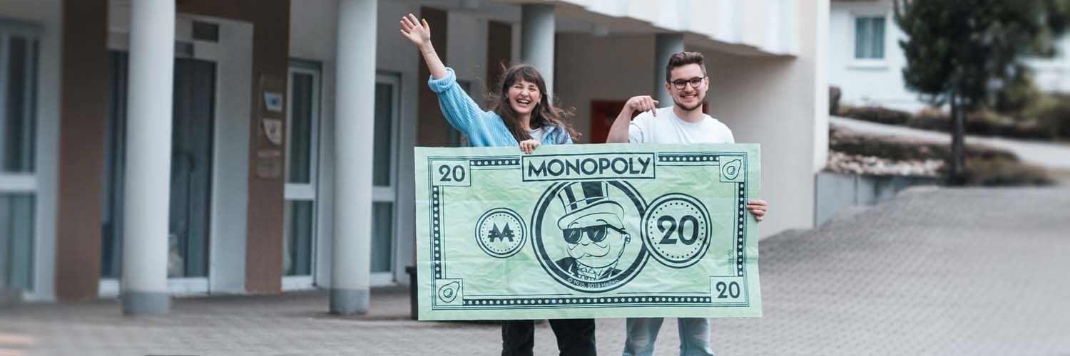 Eine Studentin und ein Student halten einen übergroßen Geldschein in der Hand.