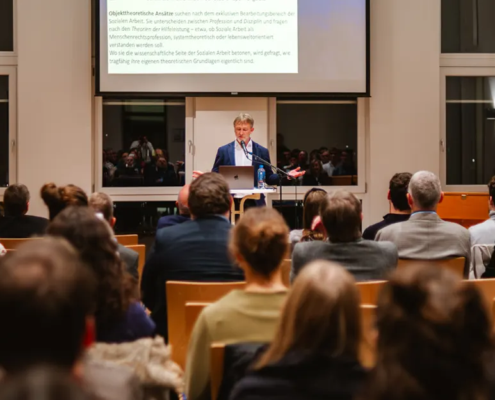 Thomas Kleber hält seine Antrittsvorlesung im Atrium des Missions- und Schulungszentrums in Bad Liebenzell. im Vordergrund ist eine große Menschenmengen, die fokussiert seinem Vortrag zuhört.