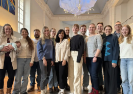 Eine 15-köpfige Gruppe aus ehemaligen Studierenden ist lächelnd auf einem Gruppenfoto zu sehen