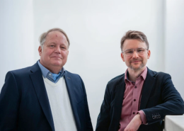 Daniel Strass und Arndt Schnepper stehen zusammen in einem Lichtdurchfluteten Gebäude.