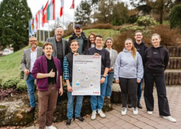 „Eine Gruppe Studierender steht gemeinsam mit Vertretern der Hochschule, der Liebenzeller Mission und Mitarbeitenden von CSL Plasma für ein Gruppenfoto. Sie halten ein Plakat mit der Aufschrift ‚Gemeinsam spenden. Ihr schafft das.‘.“