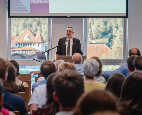 Professor David Kramer hält seine Antrittsvorlesung in den Räumlichkeiten der Internationalen Hochschule Liebenzell. Das Bild zeigt ihn an einem hellen Sommerabend vor einem großen, sitzenden Publikum im vollen Vortragssaal der IHL.