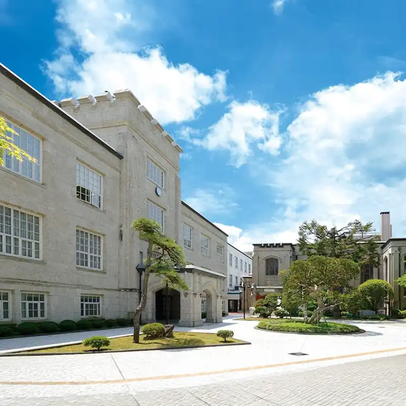 Der Campus der Tohoku Gakuin University (TGU) in Japan, einer Partnerhochschule der Internationalen Hochschule Liebenzell. Zu sehen sind helle, historische Universitätsgebäude mit Steinarchitektur, gepflegten japanischen Bäumen und Grünanlagen unter strahlend blauem Himmel.