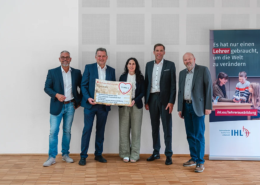 Feierliche Übergabe einer Spende in Höhe von 15.000 Euro der Sparkasse Pforzheim Calw für den Studiengang Lehrerausbildung an der Internationalen Hochschule Liebenzell. Von links nach rechts stehen Thomas Haid (Kaufmännischer Geschäftsführer der Liebenzeller Mission), der Schömberger Filialdirektor Jens Teufel, Hanna Reuther (Kanzlerin der IHL), Sven Eisele (Vorsitzender des Vorstands der Sparkasse Pforzheim Calw) und Rektor Prof. Dr. Volker Gäckle auf Holzboden vor einer weißen Wand. Sie halten gemeinsam den großen Spendenscheck. Rechts im Bild steht ein Roll-Up-Banner der IHL mit der Aufschrift: Es hat nur einen Lehrer gebraucht, um die Welt zu verändern.