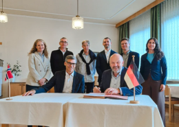 Unterzeichnung der Partnerschaftsvereinbarung (MoU) zwischen der Internationalen Hochschule Liebenzell und dem Fjellhaug International University College. Im Vordergrund sitzen der Rektor des Fjellhaug, Frank-Ole Thoresen, und der IHL-Rektor Volker Gäckle an einem Tisch mit norwegischer und deutscher Tischflagge, während die Delegationsmitglieder beider Hochschulen dahinter stehen.