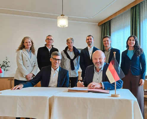 Unterzeichnung der Partnerschaftsvereinbarung (MoU) zwischen der Internationalen Hochschule Liebenzell und dem Fjellhaug International University College. Im Vordergrund sitzen der Rektor des Fjellhaug, Frank-Ole Thoresen, und der IHL-Rektor Volker Gäckle an einem Tisch mit norwegischer und deutscher Tischflagge, während die Delegationsmitglieder beider Hochschulen dahinter stehen.