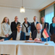 Unterzeichnung der Partnerschaftsvereinbarung (MoU) zwischen der Internationalen Hochschule Liebenzell und dem Fjellhaug International University College. Im Vordergrund sitzen der Rektor des Fjellhaug, Frank-Ole Thoresen, und der IHL-Rektor Volker Gäckle an einem Tisch mit norwegischer und deutscher Tischflagge, während die Delegationsmitglieder beider Hochschulen dahinter stehen.