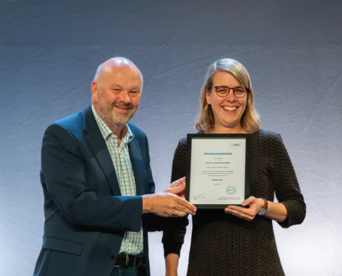 Alternativtext (Alt-Text): IHL-Rektor Prof. Dr. Volker Gäckle überreicht Frau Dr. Anna Fiona Weiß die Ernennungsurkunde zur Professorin an der Internationalen Hochschule Liebenzell. Beide stehen lächelnd nebeneinander und halten gemeinsam die gerahmte Urkunde in den Händen.