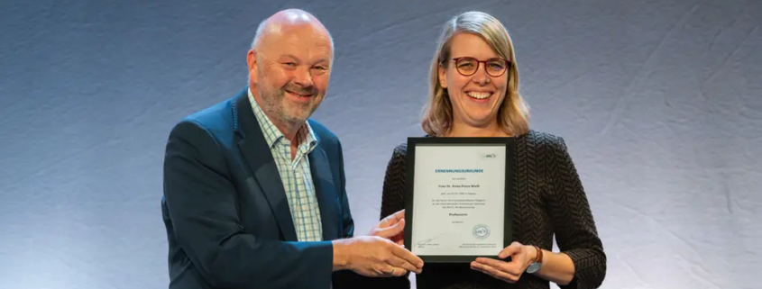 Alternativtext (Alt-Text): IHL-Rektor Prof. Dr. Volker Gäckle überreicht Frau Dr. Anna Fiona Weiß die Ernennungsurkunde zur Professorin an der Internationalen Hochschule Liebenzell. Beide stehen lächelnd nebeneinander und halten gemeinsam die gerahmte Urkunde in den Händen.